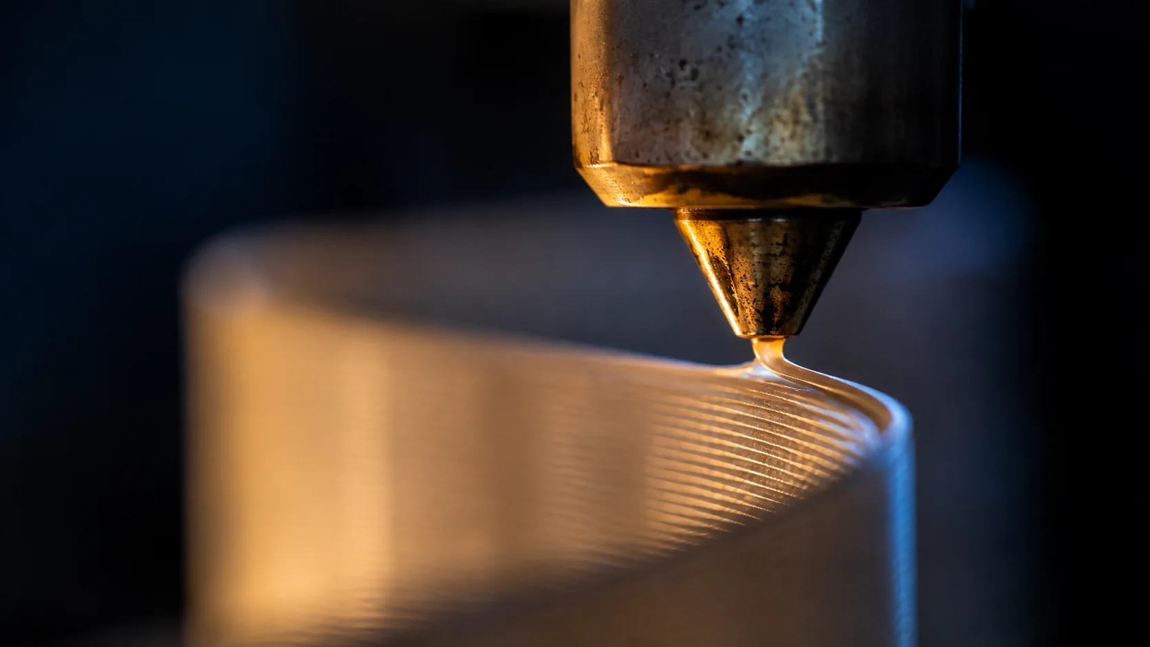 Macro of the brass nozzle laying a single line on to the top edge of a shade wall
